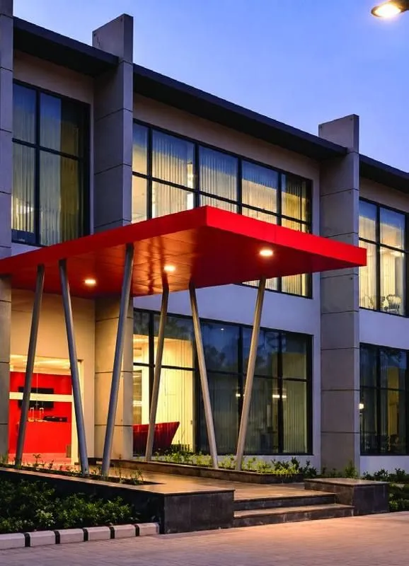 Double-height glazed entrance block with a red steel canopy at dusk