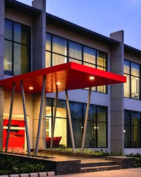 Double-height glazed entrance block with a red steel canopy at dusk